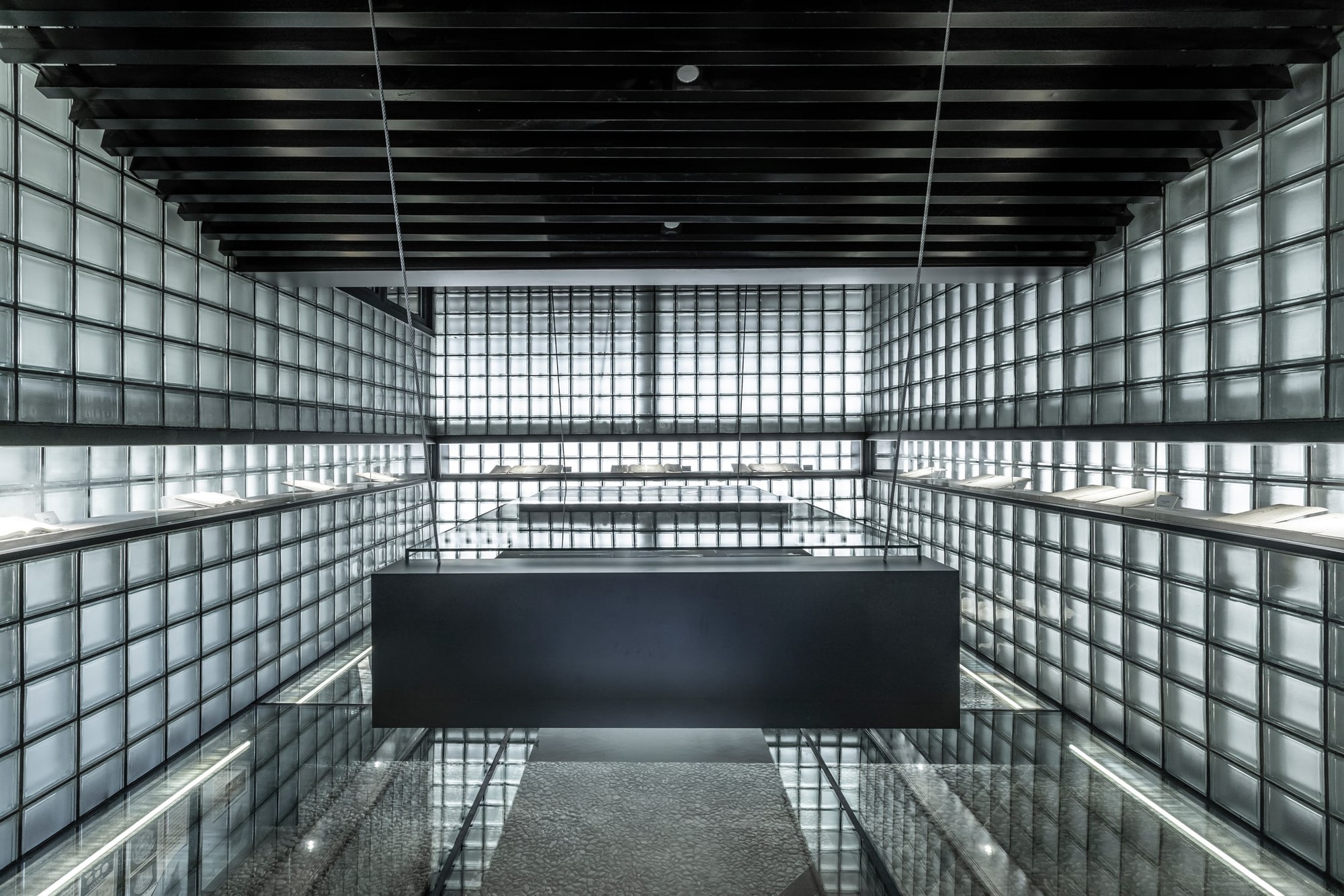 A freestanding display case above the transparent floor, seen against the glass-block walls.