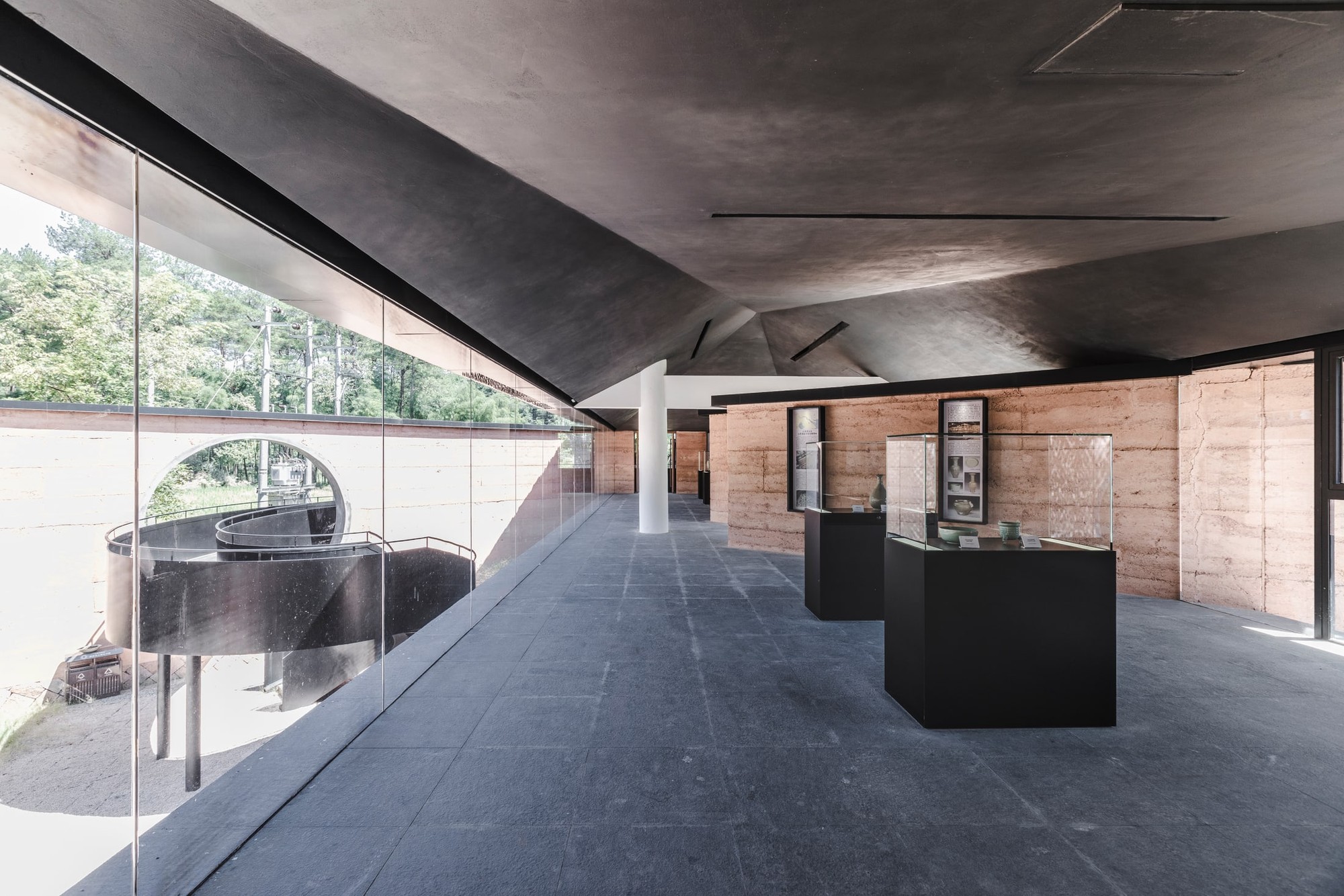 Freestanding display cases sit between the rammed earth wall and views of the surrounding landscape.