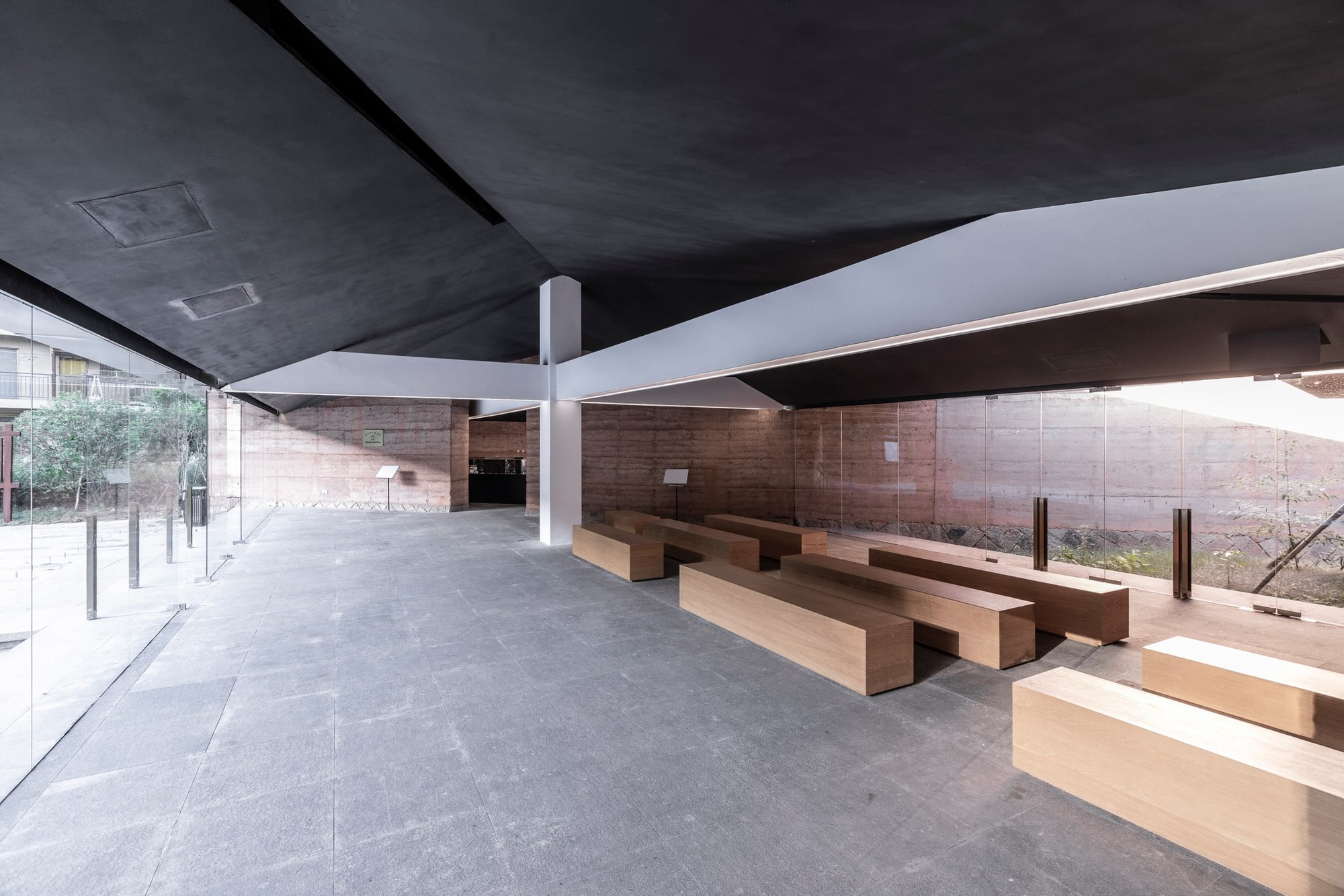 Timber seating follows the rammed earth wall beside the open glazed edge.